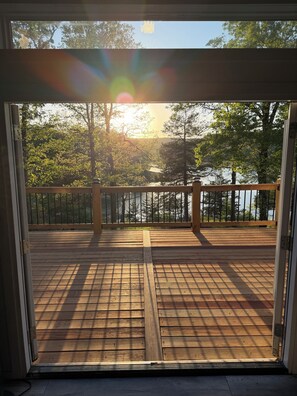 A wooden deck with a metal railing, leading to a view of trees and a body of water.