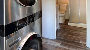 Een moderne badkamer met een ingebouwde wasmachine en droger, houten vloeren en een toilet met douchecabine.