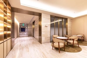 A hotel lobby with a marble floor, a reception desk, and a seating area with round tables and chairs. - Ji Hotel (Shanghai)