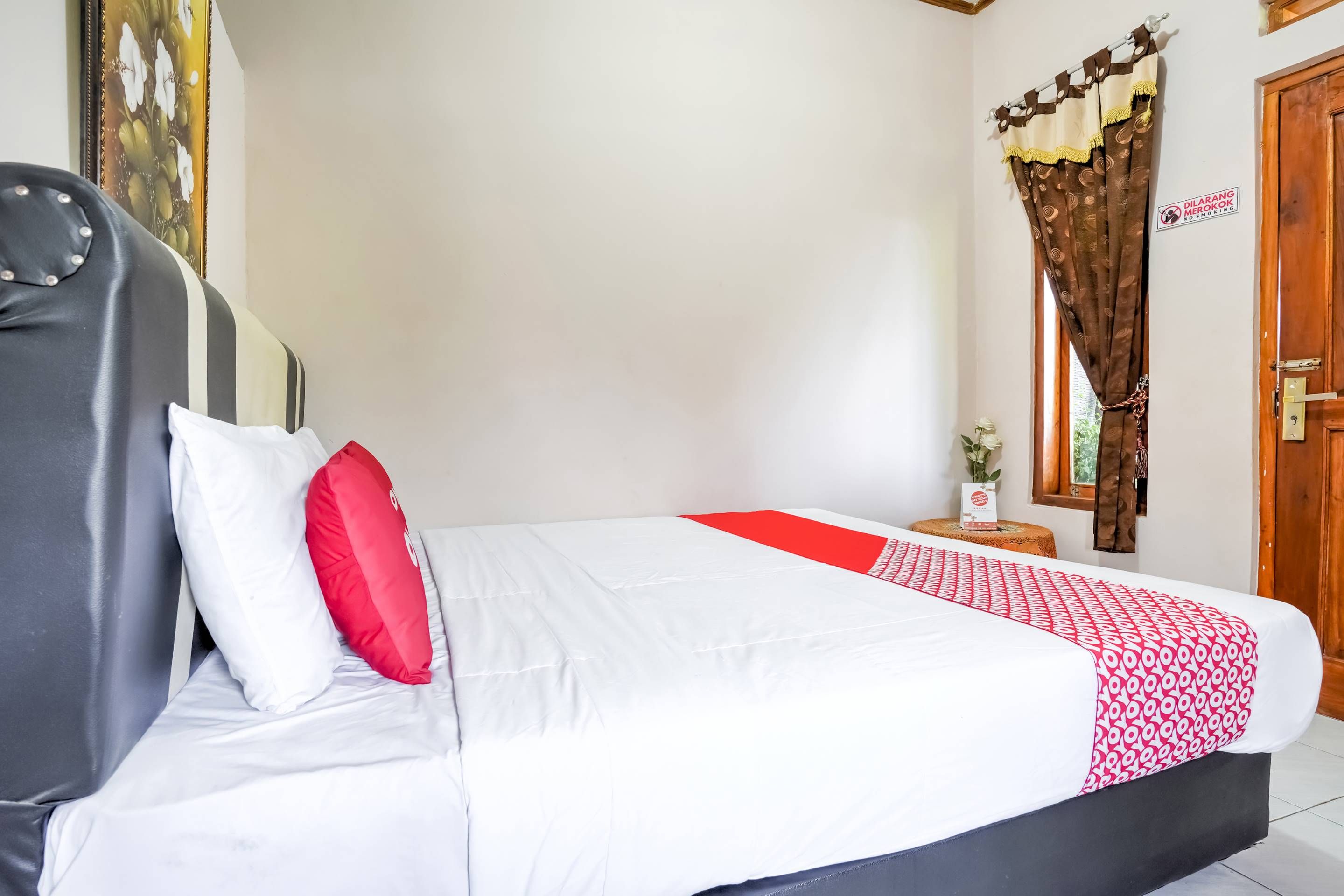 A bed with white and red bedding, a wooden headboard, and a small bedside table with a plant.