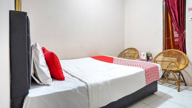 A single bed with a white and red bedspread, a black headboard, and two wicker chairs. - OYO 3509 Pondok Yanti (Ciater)