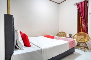 Una cama individual con una colcha blanca y roja, un cabecero negro y dos sillas de mimbre.