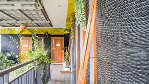 A corridor with a wooden door, potted plants, and a textured wall. - OYO 3509 Pondok Yanti (Ciater)