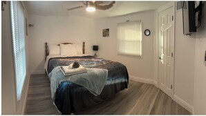 A bedroom with a bed, a nightstand, a lamp, a window with blinds, a door, and a ceiling fan. - Buckhead ridge fishing headquarters (Okeechobee)