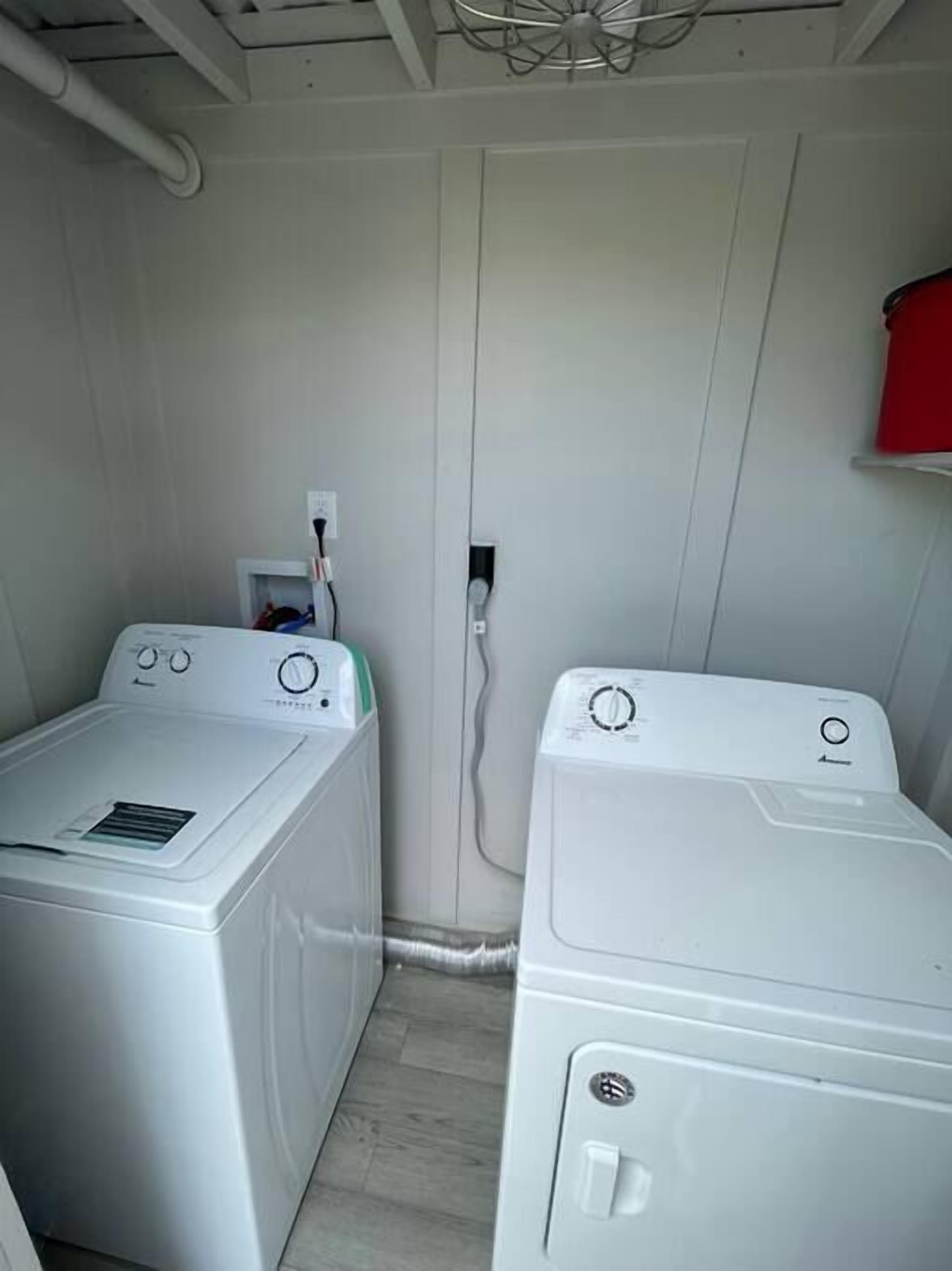Een wasserette met twee witte wasmachines, een rode kast en een plafondventilator.