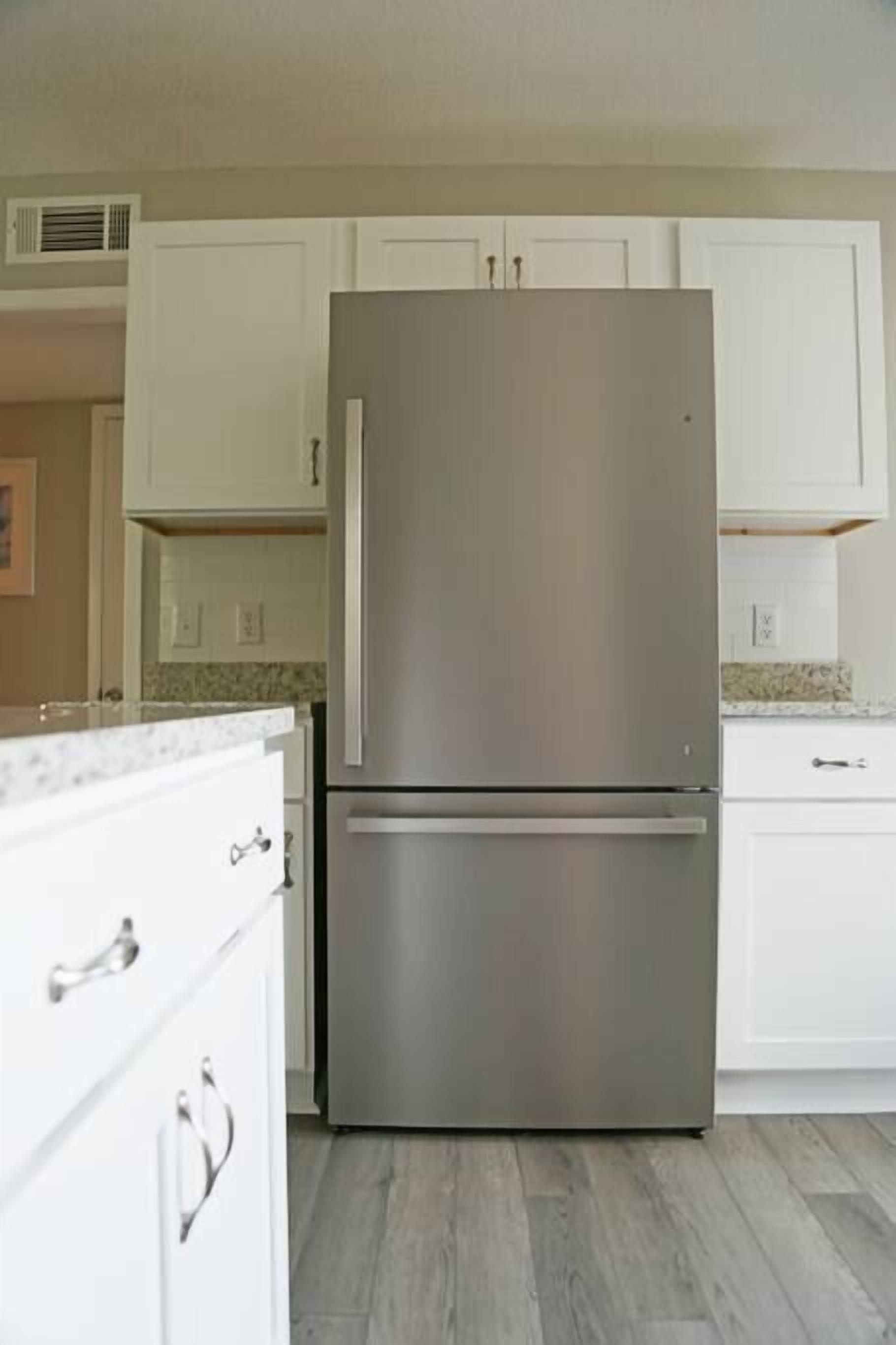 A kitchen with white cabinets, a stainless steel refrigerator, and a marble countertop.