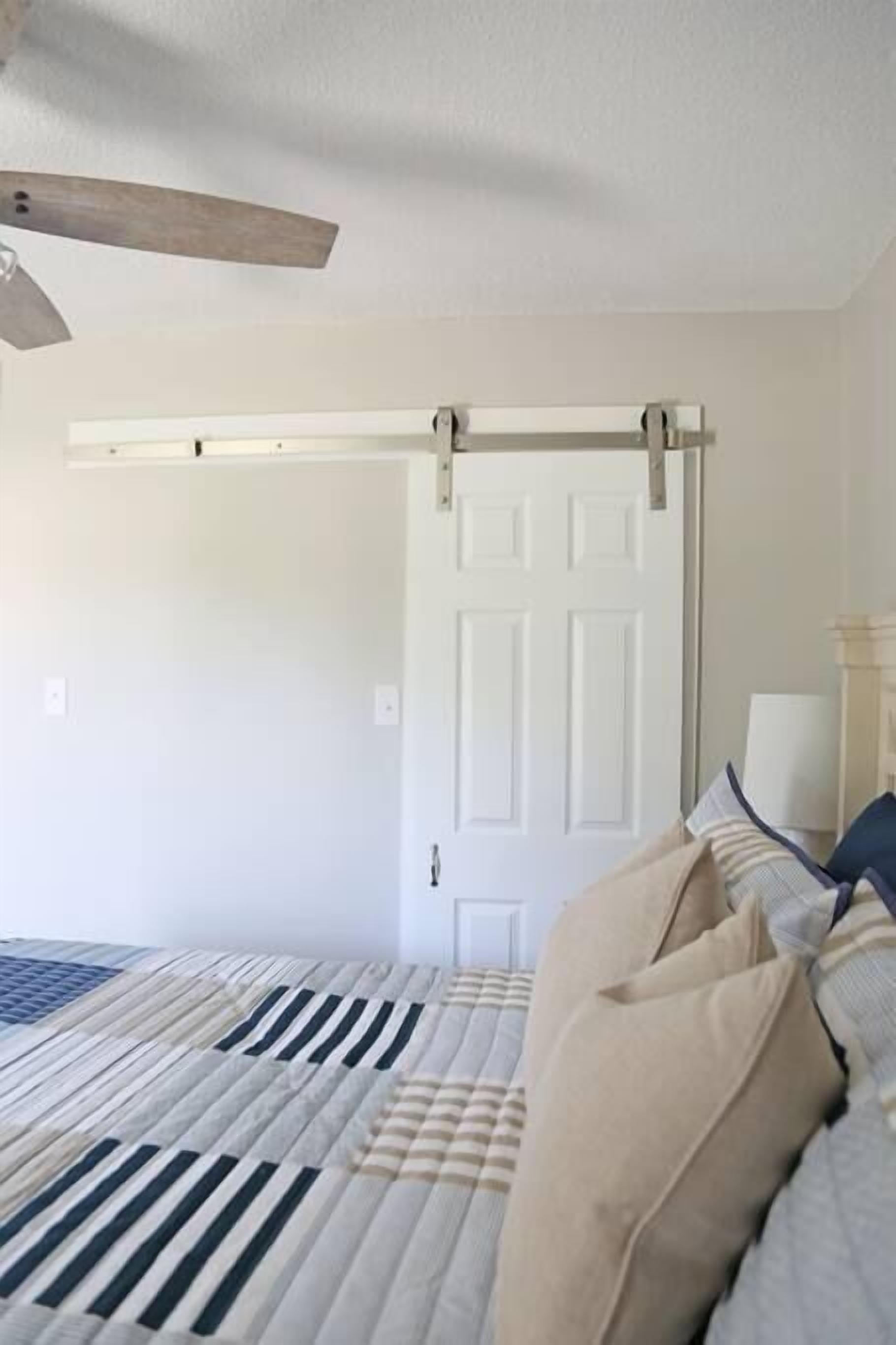 Une chambre à coucher avec un lit, un ventilateur de plafond, une porte et une fenêtre.