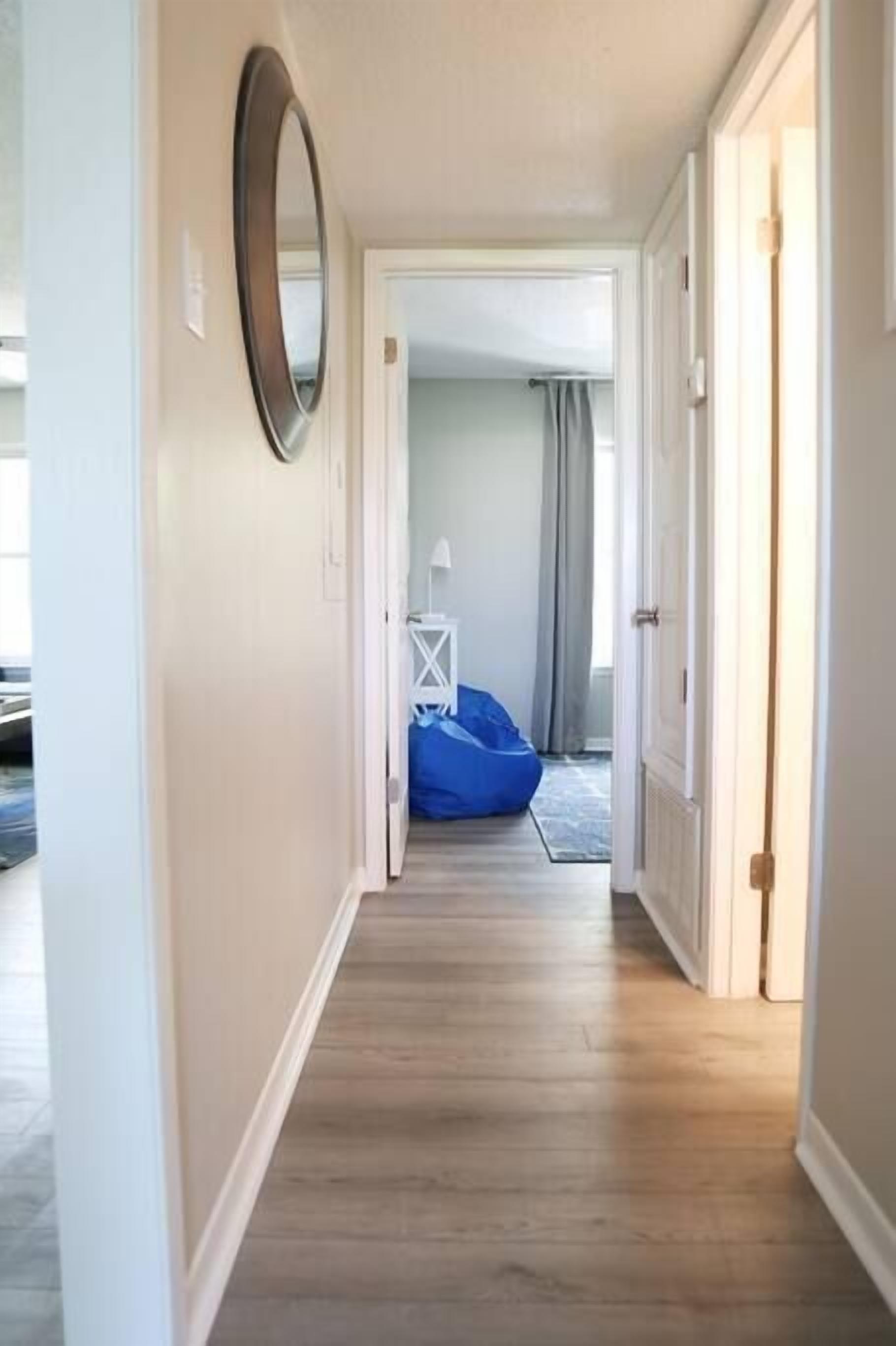 Un couloir avec un plancher en bois, un miroir sur le côté gauche et, au fond, un fauteuil en forme de poire bleu.