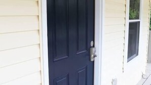 Eine dunkelblaue Tür mit weißem Rahmen, einem Klingelknopf aus Metall und einem kleinen Fenster zur rechten Seite.