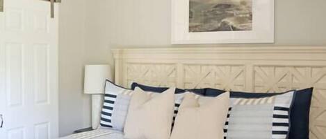A bedroom with a bed, a ceiling fan, a framed picture on the wall, and a door.