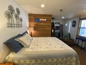 A bedroom with a bed, a wooden headboard, a wall clock, and a window with blinds. - Billy's Bunkhouse Downtown Bandera, TX. (Bandera)