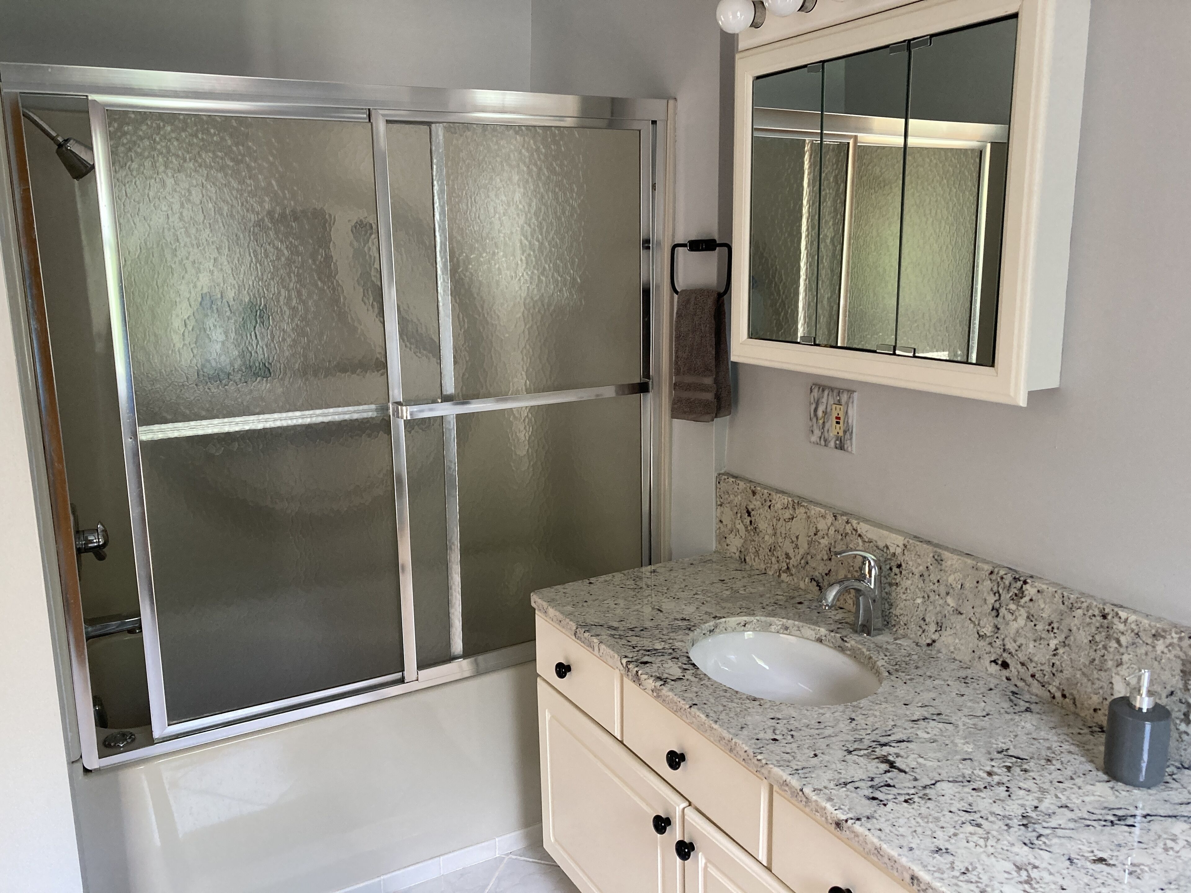 A bathroom with a glass-enclosed shower, a sink with a marble countertop, and a mirror above the sink.