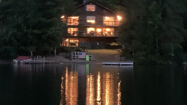 Une maison à plusieurs étages, dotée d’un quai et de bateaux, entourée d’une forêt dense.