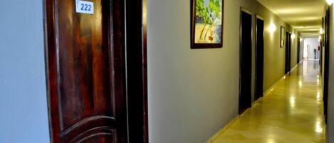 Un pasillo de hotel con una puerta de madera con el número 222, un cuadro enmarcado en la pared y un piso pulido.