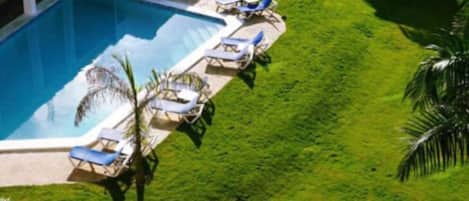 An aerial view of a swimming pool with lounge chairs and a well-maintained lawn.