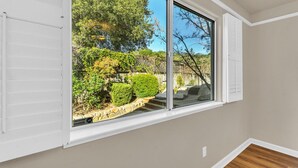 Ein Zimmer mit großem Fenster und Blick auf einen Garten mit Bäumen und einem Kiesweg.