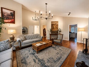 A living room with a sofa, armchair, coffee table, and a rug. There is a painting on the wall, a chandelier, and a lamp. - Spacious Oasis Hot Tub Backyard Garden 3BR/2BA (Sonoma)