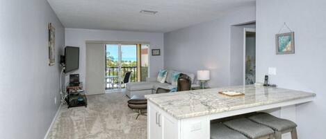A modern kitchen with a marble countertop, bar stools, and a view to the outside.