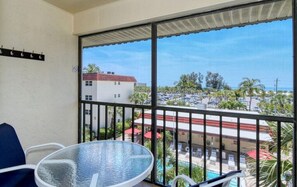 Enjoy the view from this balcony with a glass table and two chairs, overlooking the parking lot and adjacent building.