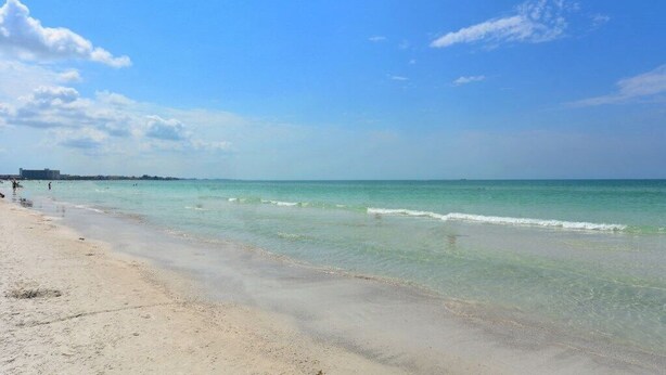 A beach with clear turquoise water, a sandy shore, and a distant city skyline. - Condo# 415 2 Bed/1 bath Condo Steps to Siesta Key Beach! (Sarasota)