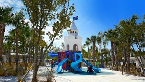 A playground with a white tower and blue slides, surrounded by palm trees. - Condo# 415 2 Bed/1 bath Condo Steps to Siesta Key Beach! (Sarasota)