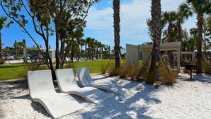 Outdoor lounge chairs on a sandy area with palm trees and a clear sky. - Condo# 415 2 Bed/1 bath Condo Steps to Siesta Key Beach! (Sarasota)