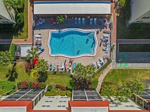 An aerial view of a hotel with a swimming pool surrounded by lounge chairs and umbrellas.