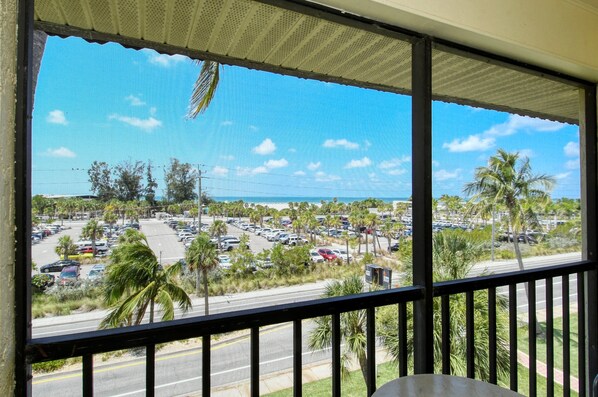 A view from a balcony overlooking a parking lot with palm trees and a clear sky.