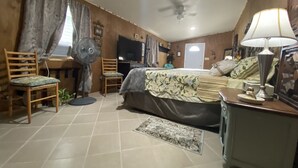 A bedroom with a bed, a chair, a TV, a fan, and a lamp. - Hilda’s Garage Bandera, TX (Bandera)