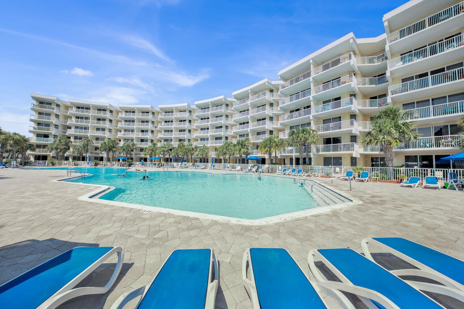 A hotel with a large pool, multiple balconies, and sun loungers.
