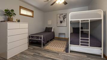 A bedroom with a bunk bed, a desk with drawers, a small bedside table, a potted plant, a framed picture, and a patterned rug.