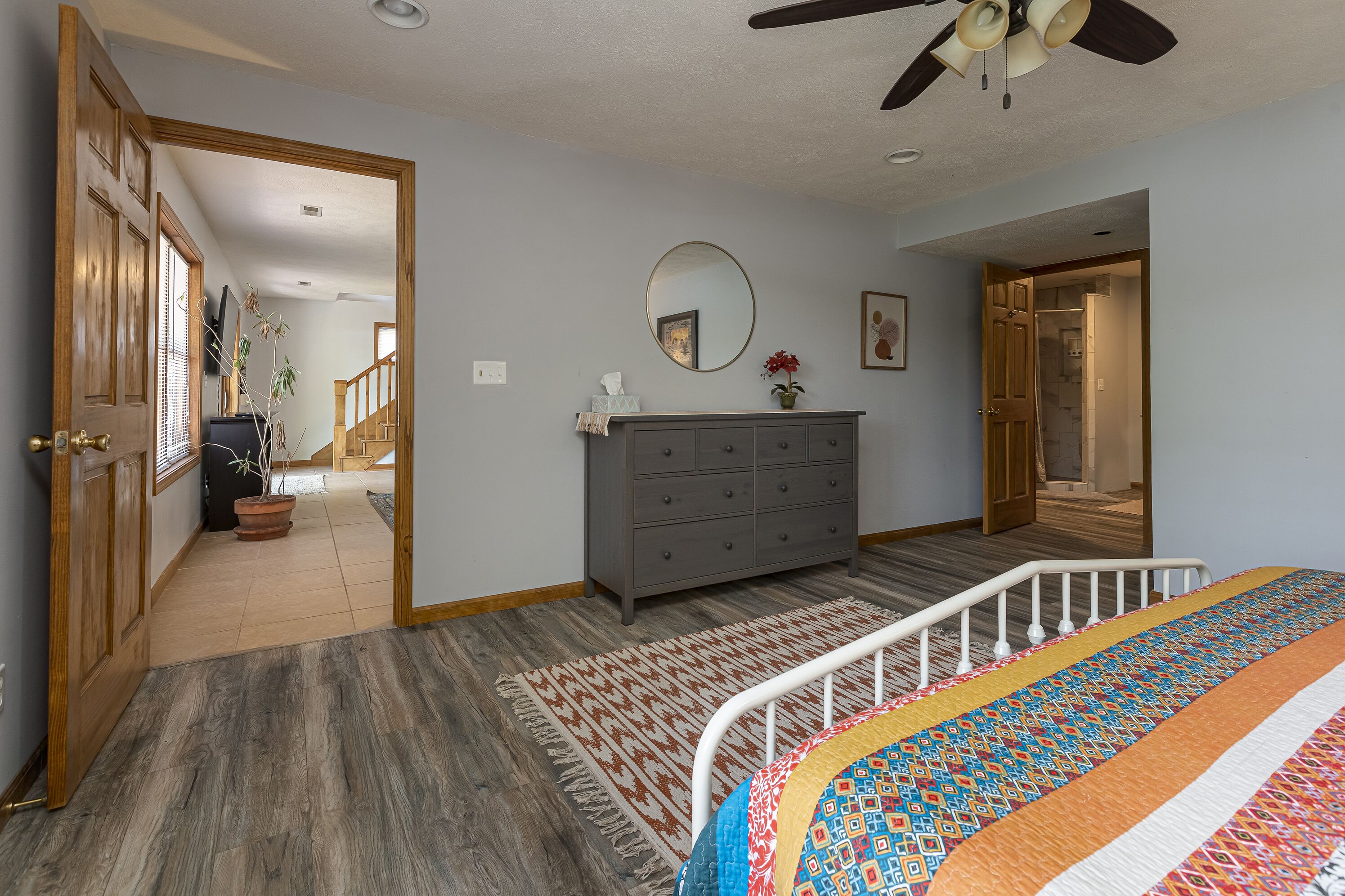 Un dormitorio con cama, cómoda y espejo. Hay una puerta que da a otra habitación.