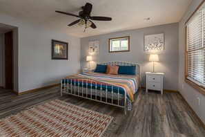 A bedroom with a bed, two bedside tables, a ceiling fan, and a window with blinds.