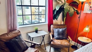 A cozy room with a leather armchair, a small table with a plant, a large potted plant, a lamp, and a view through a window. - FANTASTIC LOCATION NEAR ALL ATTRACTIONS! (Orlando)