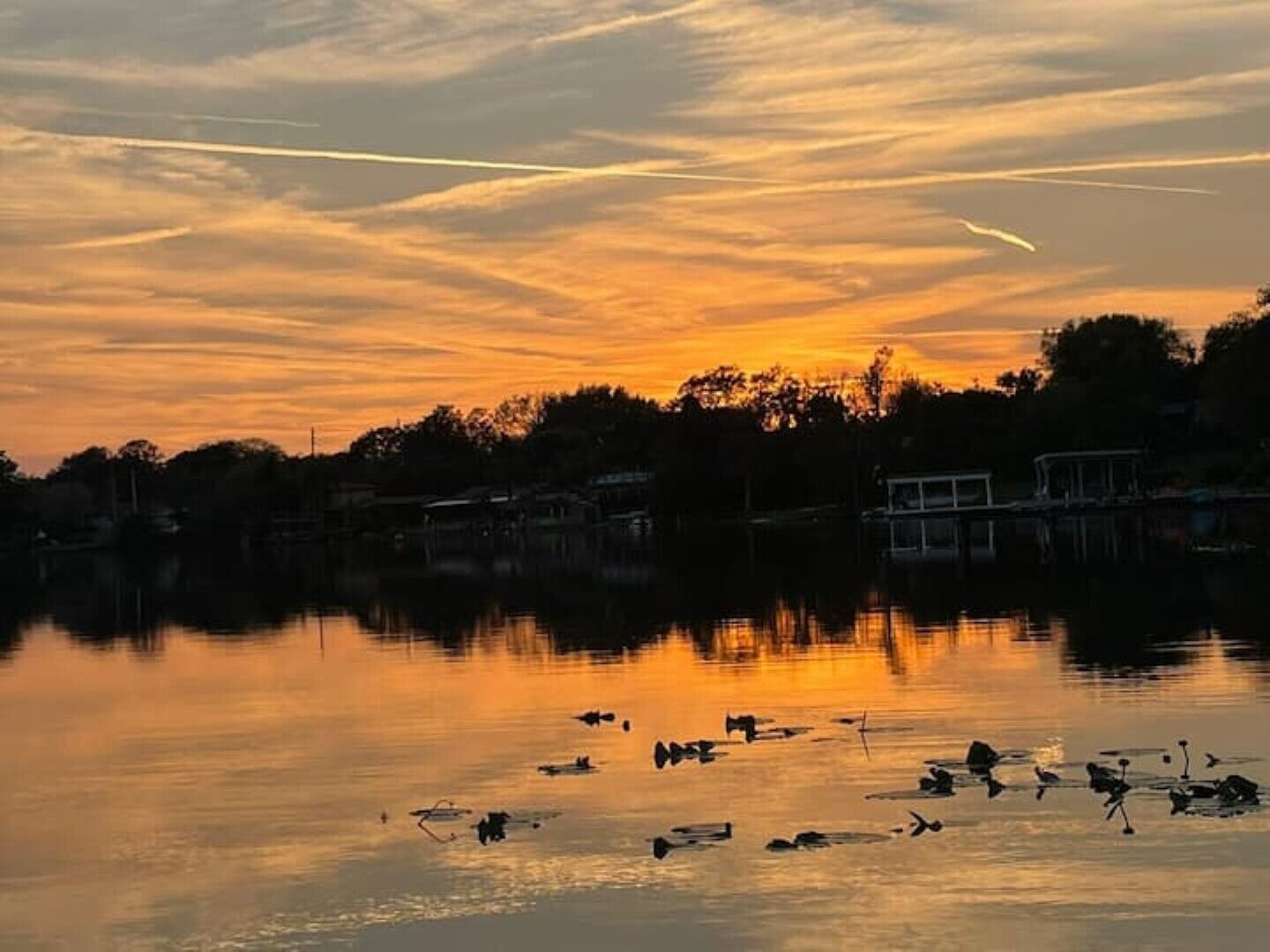 A sunset over a calm lake with boats and a dock in the foreground.