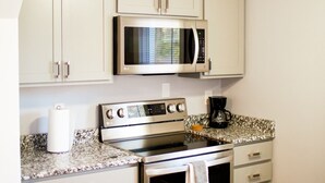 A compact kitchen with white cabinets, a microwave, a stove, and a coffee maker.
