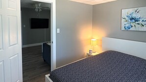 A bedroom with a bed, a TV, a ceiling fan, a lamp, and a painting on the wall.
