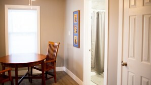 A dining area with a round table and wooden chairs, a ceiling fan, and a door leading to another room.