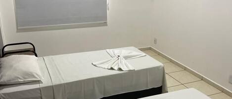 A hotel room with two beds, a flat-screen TV, an air conditioning unit, and a window with blinds.