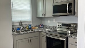 A kitchen with grey cabinets, a stainless steel oven, a microwave, and a window with blinds.