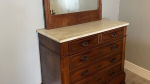 A wooden dresser with a mirror and drawers against a wall.