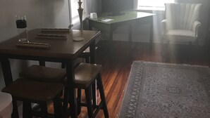 A room with a wooden dining table, two chairs, a lamp, a television, and a white armchair.