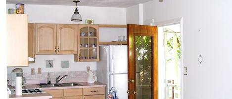 Una cocina con armarios de madera, un refrigerador, un ventilador de techo y una puerta que da a un balcón.