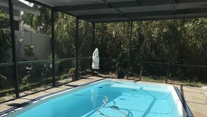 A swimming pool with a clear blue water, surrounded by a tiled deck and a covered area with a glass roof.