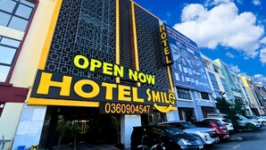 A hotel with a prominent 'OPEN NOW' sign, a contact number, and a large windowed facade.