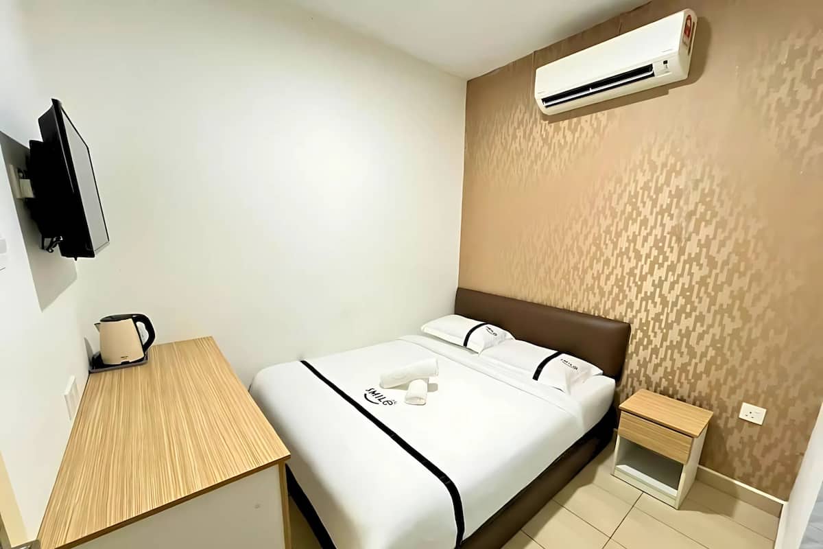 A hotel room with a bed, a bedside table, a small nightstand, a wall-mounted air conditioner, and a television on the wall.