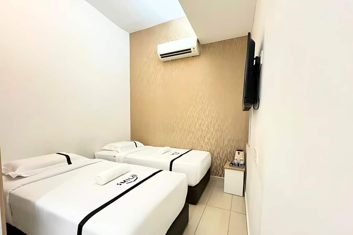 A hotel room with two beds, a TV mounted on the wall, and an air conditioning unit above the beds.