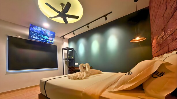 A modern hotel room with a bed, a flat-screen TV, a ceiling fan, and a wall-mounted shelf.