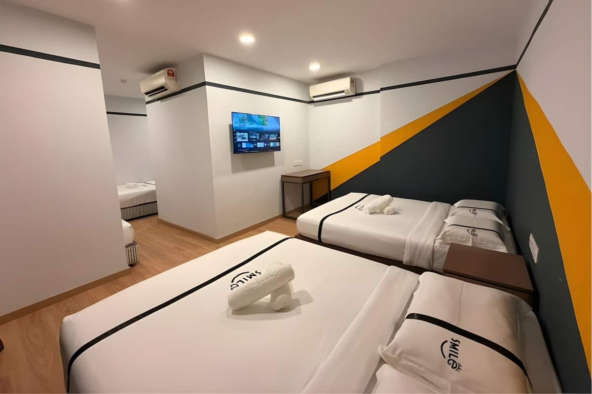 A hotel room with two beds, a TV mounted on the wall, and air conditioning units.