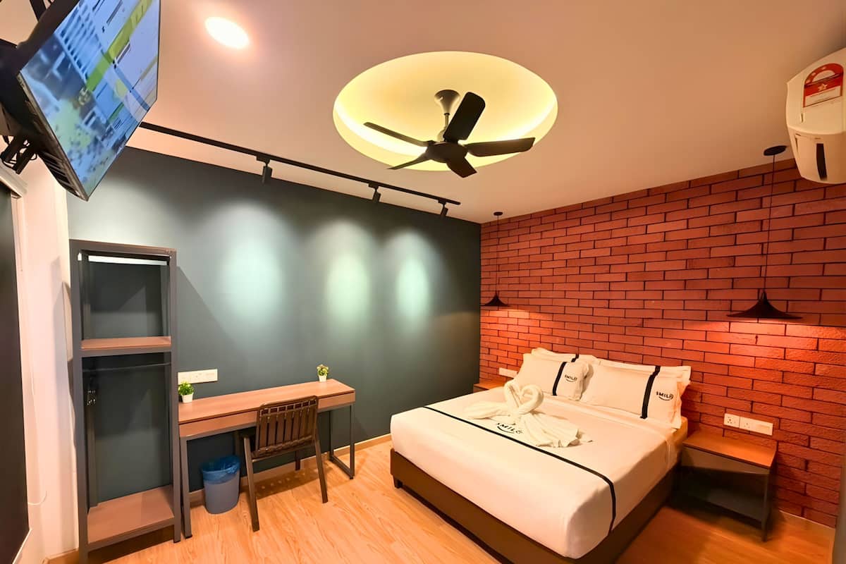 A modern hotel room with a bed, desk, chair, and a ceiling fan.